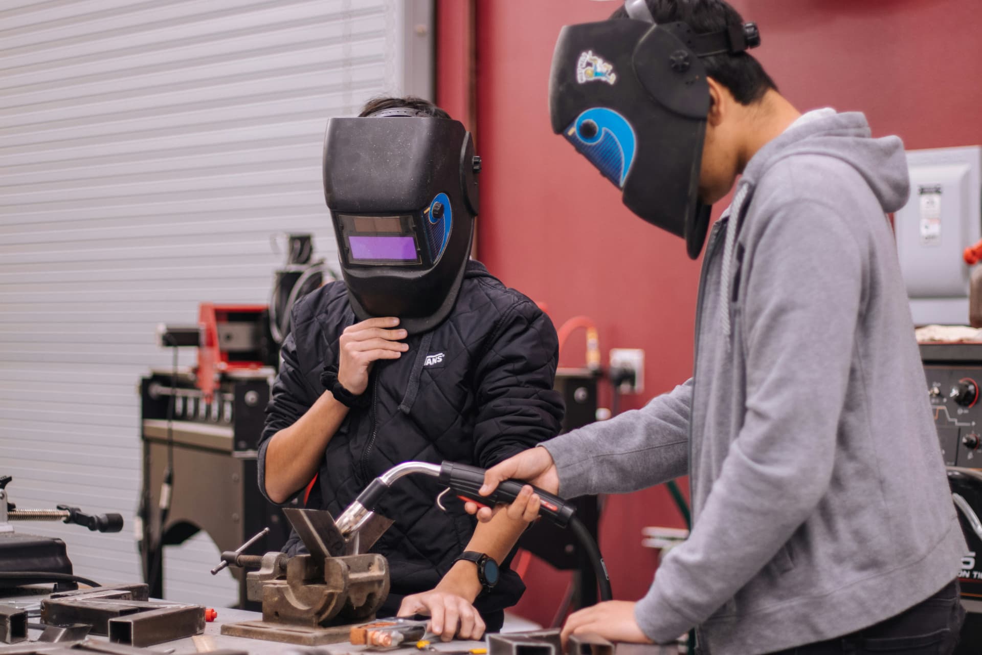 Two people learning metalworking with welding masks