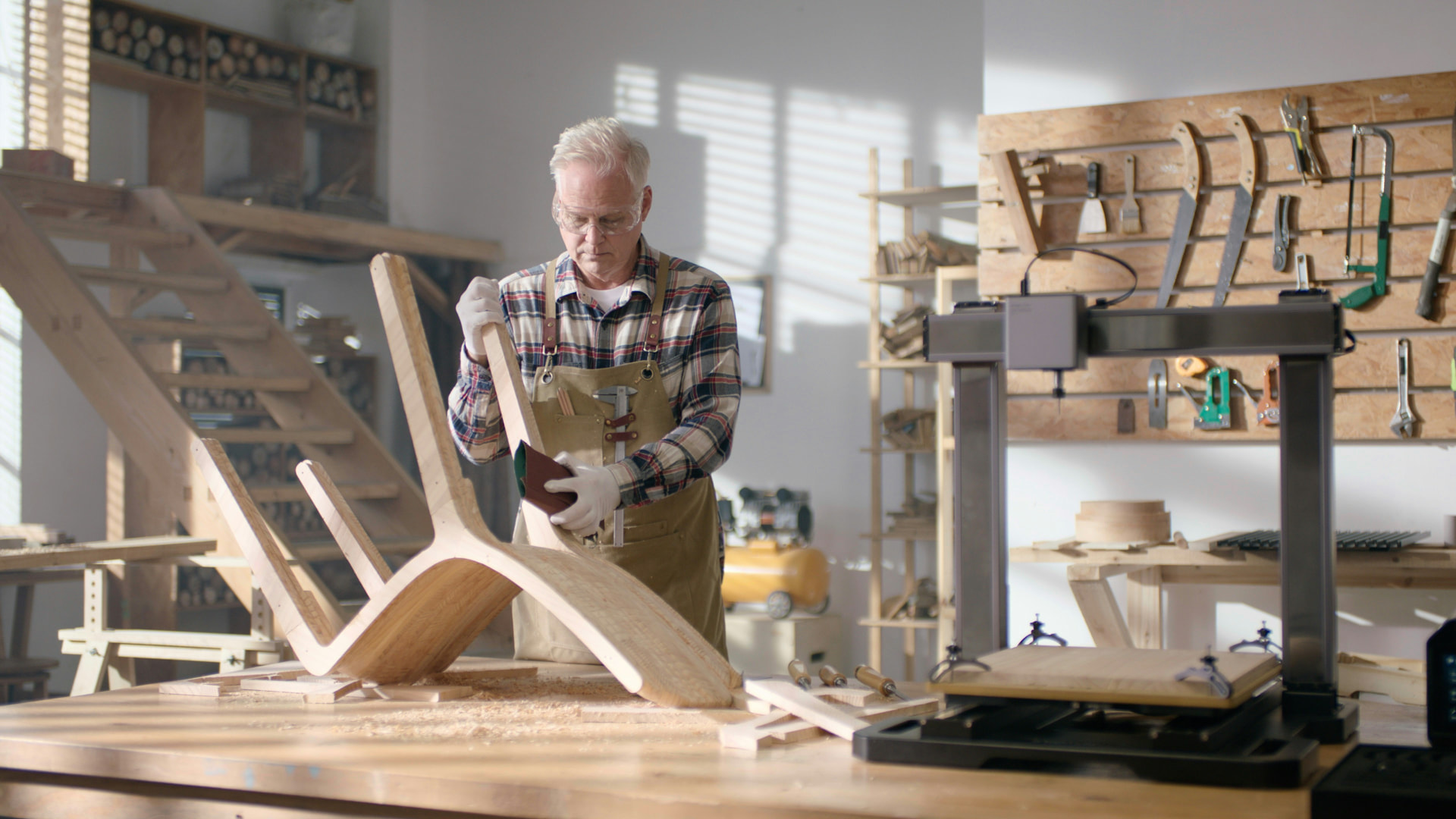 A woodworker sanding a handmade chair in a bright workshop